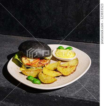 Unique black bun burger with seasoned potato wedges on plate Unique black bun burger with seasoned potato wedges on plate 123653523