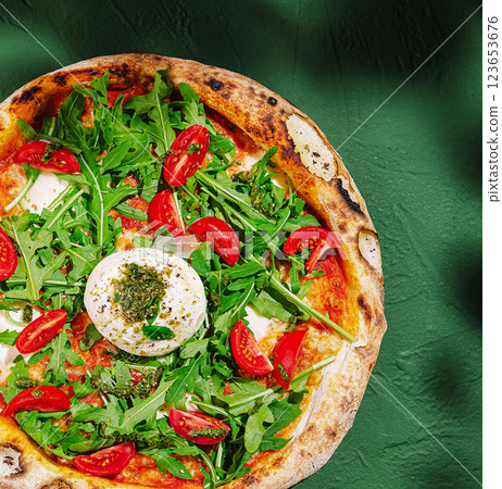 Fresh pizza topped with arugula and cherry tomatoes on a green table Fresh pizza topped with arugula and cherry tomatoes on a green table 123653676