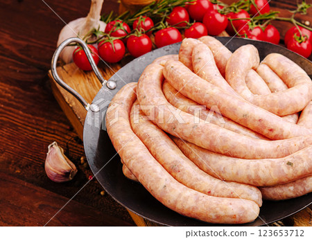 Fresh sausages prepared for grilling with herbs and tomatoes 123653712