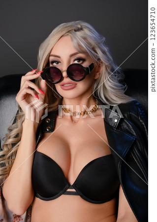Confident woman in stylish lingerie and sunglasses poses on a leather chair Confident woman in stylish lingerie and sunglasses poses on a leather chair 123654710