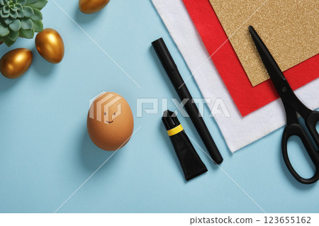 A DIY Easter egg with a smiling face on a background of art supplies. Crafting accessories. A DIY Easter egg with a smiling face on a background of art supplies. Crafting accessories. 123655162