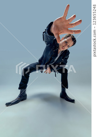 Charismatic performer reaching forward with intense gaze and dynamic posture against gradient background. 123655248