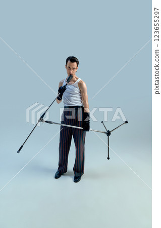 Young singer gripping microphone stand with intense focus, exuding timeless stage confidence against gradient studio setting. Vintage charisma. Young singer gripping microphone stand with intense focus, exuding timeless stage confidence against gradient studio setting. Vintage charisma. 123655297