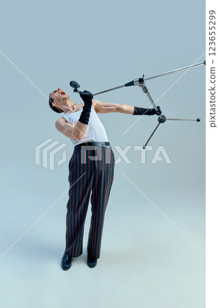 Talented vocalist pushing boundaries, microphone stand twisting mid-air in dramatic moment of musical expression against studio backdrop. Talented vocalist pushing boundaries, microphone stand twisting mid-air in dramatic moment of musical expression against studio backdrop. 123655299
