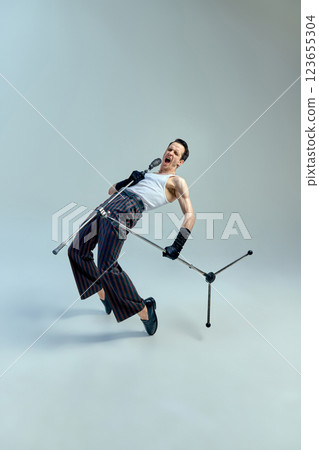 Rock-inspired energy. Stylish singer leaning back into performance with raw passion and dramatic intensity against gradient studio background. Rock-inspired energy. Stylish singer leaning back into performance with raw passion and dramatic intensity against gradient studio background. 123655304