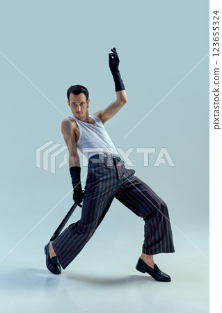 Dynamic performer striking powerful pose with intense gaze, gripping microphone in expressive dance motion against soft-toned studio background. Dynamic performer striking powerful pose with intense gaze, gripping microphone in expressive dance motion against soft-toned studio background. 123655324