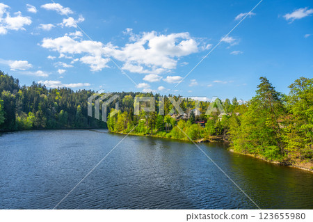 A tranquil setting at Pastviny Water Reservoir, surrounded by lush green forests and clear blue skies. Visitors enjoy nature and the serene landscape in the beautiful Czech countryside. 123655980