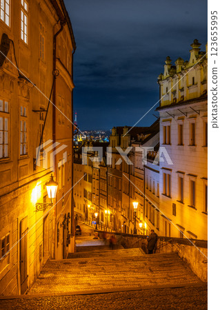 The charming staircase leading to Prague Castle is bathed in warm yellow light. Surrounding buildings create a cozy atmosphere, while the night sky adds depth to the scene. The charming staircase leading to Prague Castle is bathed in warm yellow light. Surrounding buildings create a cozy atmosphere, while the night sky adds depth to the scene. 123655995