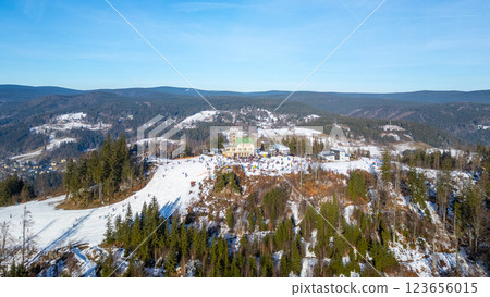 Enjoy a stunning aerial view of Tanvaldsky Spicak Ski resort in Czechia during winter. Snow-covered slopes and vibrant trees surround the bustling resort area, inviting outdoor fun. 123656015