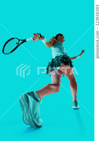 Creative collage. Tennis player dressed in turquoise executing powerful swing, motion captured from dynamic low angle. Vibrant colors. Creative collage. Tennis player dressed in turquoise executing powerful swing, motion captured from dynamic low angle. Vibrant colors. 123656303