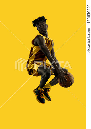 Dynamic composition. Young African-American man, basketball player mid-air, intense jump creating perfect moment of action. Slam dunk. Vibrant yellow. Dynamic composition. Young African-American man, basketball player mid-air, intense jump creating perfect moment of action. Slam dunk. Vibrant yellow. 123656305