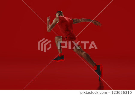 Dynamic composition. Sprinter in red accelerating into motion, power and agility radiating against vivid background. Concept of sport Dynamic composition. Sprinter in red accelerating into motion, power and agility radiating against vivid background. Concept of sport 123656310