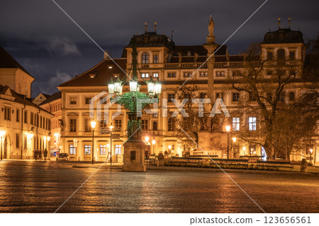 In the evening, the historic lamppost at Hradcanske Square casts a warm glow over the cobblestone streets. Surrounding buildings reflect light, enhancing the lively atmosphere of Prague. 123656561