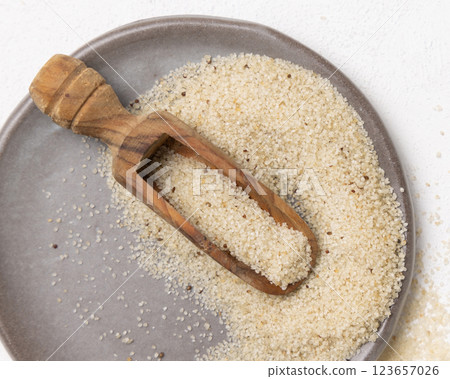 Raw uncooked fonio seeds on grey plate with a wooden scoop on white table topview. African cereal Raw uncooked fonio seeds on grey plate with a wooden scoop on white table topview. African cereal 123657026