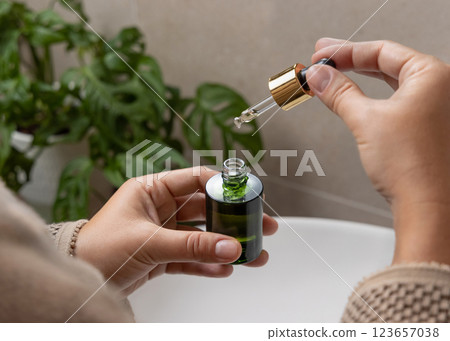 Closeup of woman hands opening green dropper bottle aginst green plant, drop falling from pipette Closeup of woman hands opening green dropper bottle aginst green plant, drop falling from pipette 123657038