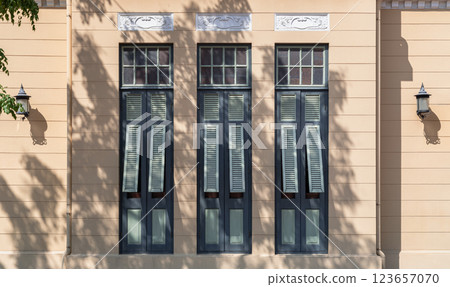 The Sunlight shines through Multiple green wooden louvered window shutters on cement wall. 123657070