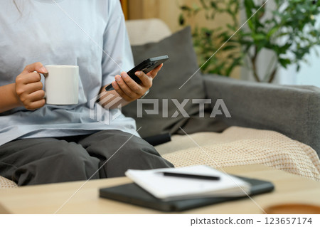 Cropped shot young woman in casual clothes using mobile phone on sofa Cropped shot young woman in casual clothes using mobile phone on sofa 123657174