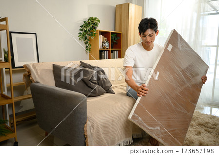 Man unwrapping a wooden table panel during a furniture assembly in living room 123657198