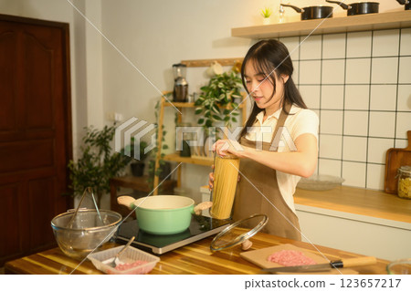 Pretty asian woman preparing to cook spaghetti in a cozy kitchen Pretty asian woman preparing to cook spaghetti in a cozy kitchen 123657217