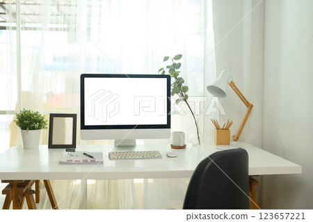 Desktop computer with blank screen, desk lamp, documents, coffee mug and decorative plants 123657221