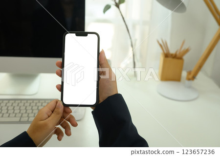 Close up of businessperson holding smartphone with white screen sitting at desk 123657236