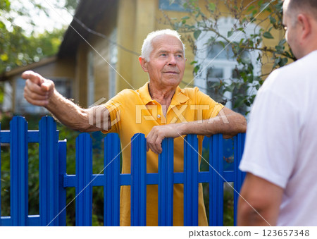 Neighbor conversation. Two smiling men breezily chatting near fence of rural house 123657348