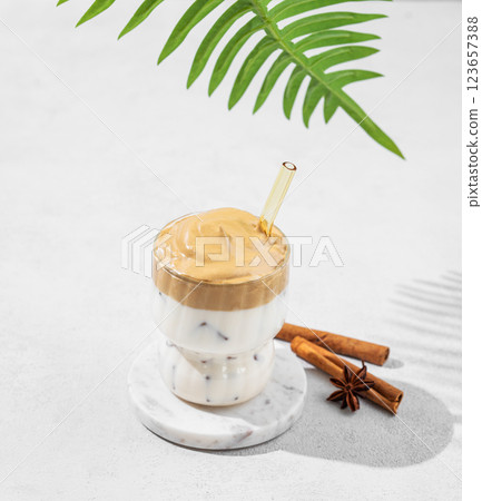 Dalgona coffee in a glass on a white textured background with palm leaf, spices and sunlight. Dalgona coffee in a glass on a white textured background with palm leaf, spices and sunlight. 123657388