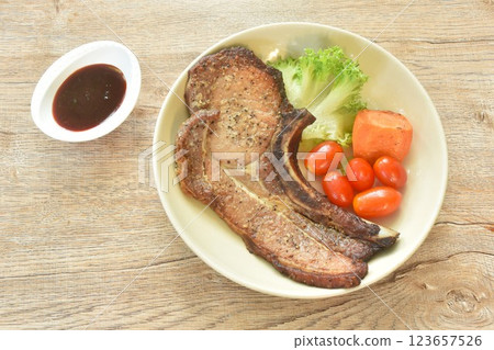 grilled black pepper pork chop steak and lettuce with tomato couple boiled carrot on plate dipping barbecue sauce in cup grilled black pepper pork chop steak and lettuce with tomato couple boiled carrot on plate dipping barbecue sauce in cup 123657526