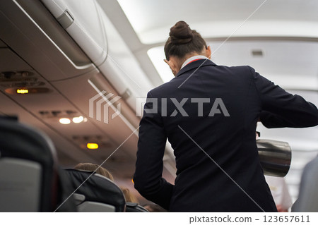 An unrecognizable flight attendant pours tea and serves hot drinks on board the plane. View of the ceiling in the hallway of the plane. High quality photo 123657611