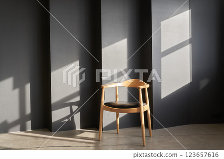 There is sunlight on the black uneven wall. With space to copy. A wooden chair with a rounded shape and design stands against a dark wall. High quality photo There is sunlight on the black uneven wall. With space to copy. A wooden chair with a rounded shape and design stands against a dark wall. High quality photo 123657616