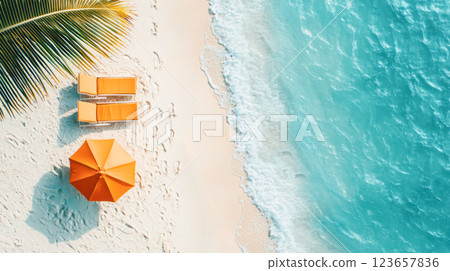 Top view of a tropical beach with two orange lounge chairs and a matching umbrella on soft white sand, next to turquoise ocean waves. 123657836