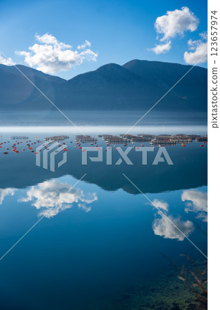 Mountains with clouds and their reflection in the still waters of the sea, separated by a strip of fog in winter morning Bay of Kotor in Montenegro Mountains with clouds and their reflection in the still waters of the sea, separated by a strip of fog in winter morning Bay of Kotor in Montenegro 123657974