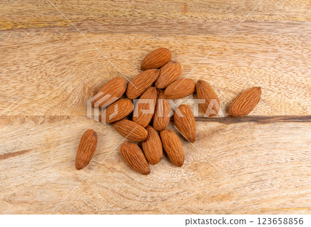 Almonds pile, nut group, whole almond seeds, brown scattered fruit kernels, dry raw nuts on wood 123658856