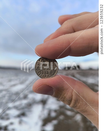 An old silver coin, a hand holding an ancient silver coin in a field. An ancient coin in your hands. An old silver coin 123659232