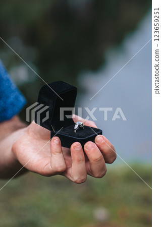Close up of man hands holding engagement ring box on the beach 123659251