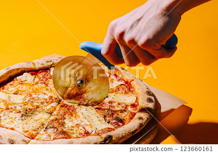 Hand using pizza cutter to slice fresh pizza on orange background Hand using pizza cutter to slice fresh pizza on orange background 123660161