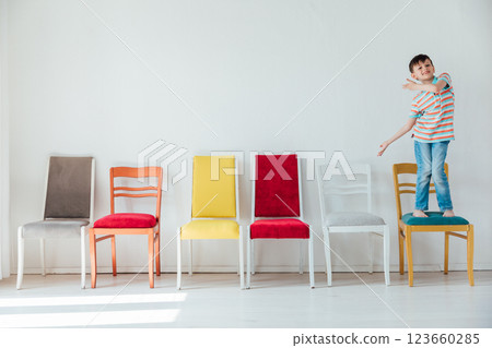 Little Boy Jumping On Chairs In White Room Interior Little Boy Jumping On Chairs In White Room Interior 123660285