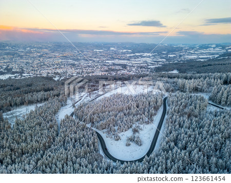 A beautiful winter evening captures a panoramic view above Liberec City, Czechia. Snow-covered trees blanket the landscape, while a winding road meanders through the serene setting. 123661454