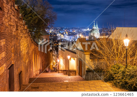 The staircase leading to Prague Castle sparkles under the night sky. Vintage lamps line the path, casting a warm glow on the cobblestones, revealing the cityscape's beauty below. 123661465