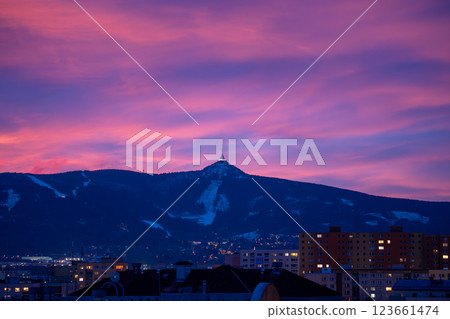 Jested Mountain stands majestically against a vibrant winter sky. The evening hues of pink and purple illuminate the snow-capped peak, creating a breathtaking backdrop for the nearby town. Jested Mountain stands majestically against a vibrant winter sky. The evening hues of pink and purple illuminate the snow-capped peak, creating a breathtaking backdrop for the nearby town. 123661474