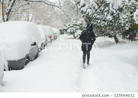 Urban Street Covered in Snow with Parked Cars and Person Walking 123664032
