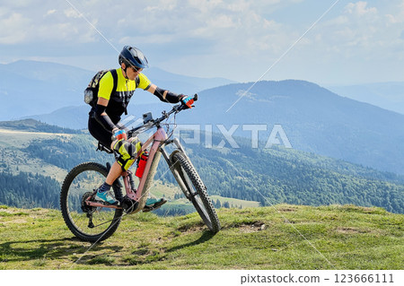 Cyclist man riding electric mountain bike outdoors. Male tourist biking along grassy trail in the mountains, wearing helmet and backpack. Concept of sport, active leisure and nature. 123666111