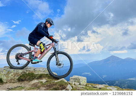 Cyclist man riding electric mountain bike outdoors. Male tourist biking along grassy trail in the mountains, wearing helmet. Concept of sport, active leisure and nature. Cyclist man riding electric mountain bike outdoors. Male tourist biking along grassy trail in the mountains, wearing helmet. Concept of sport, active leisure and nature. 123666152