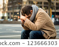 A worried man with his head bowed sits on the street of a big city, generative ai 123666303