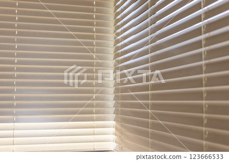 Beige wooden blinds, close-up view, covering a window, with soft sunlight filtering through slats 50mm. Wood blinds create a pattern of light and shadow, adding warmth and texture to interior space. 123666533