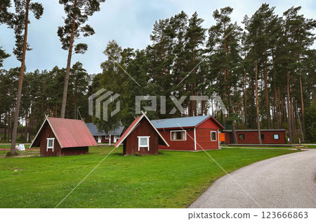 A row of small red houses are in a grassy field. 123666863