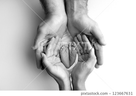 A father and mother hold the feet of a newborn child in a blanket. The feet of a newborn in the hands of parents. Black and white Photo of foot, heels and toes. The palms of the parents. 123667631