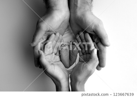 A father and mother hold the feet of a newborn child in a blanket. The feet of a newborn in the hands of parents. Black and white Photo of foot, heels and toes. The palms of the parents. 123667639