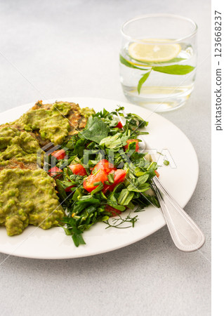 Enjoy a healthy breakfast with zucchini pancakes topped with green pea pesto, served with a mixed salad of fresh seasonal vegetables and herbs for a nutritious start 123668237