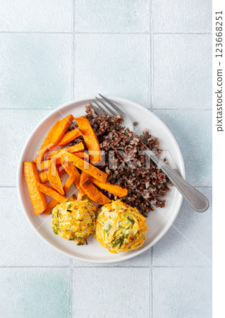 A healthy and filling meal of brown rice, baked sweet potato and squash chickpea pancakes, packed with flavor and nutrients, fresh salad of tomatoes and cucumbers 123668251